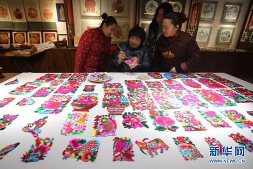 1月29日，在承德市双桥区俊凤剪纸创作室，剪纸艺人石俊凤（中）与同事交流剪纸作品的上色技巧。