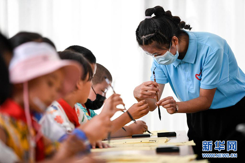 7月30日，返乡大学生志愿者（右一）在宁夏银川市兴庆区掌政镇新创家园社区为学生指导毛笔握持姿势。