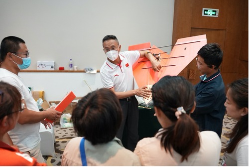 图为：教师们围绕专家聆听遥控纸飞机的试飞要点