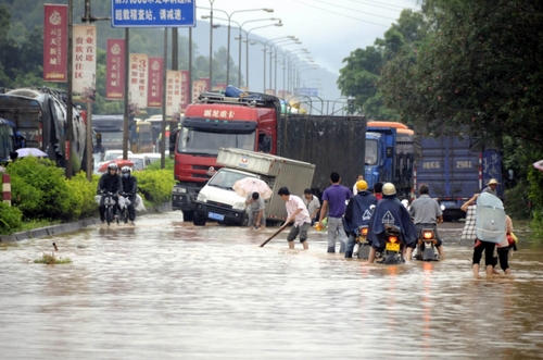 5月18日，国道324线广西兴业县石南镇黑石岭路段被洪水淹没，一名群众手持木棍为摩托车探路。