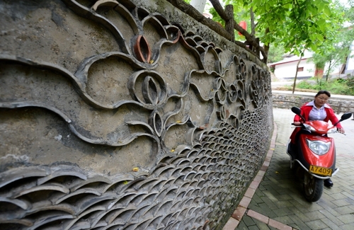 5月27日，在甘肃省陇南市康县王坝乡大水沟村，一名村民驾车从用废旧瓦片装饰的花坛旁走过。