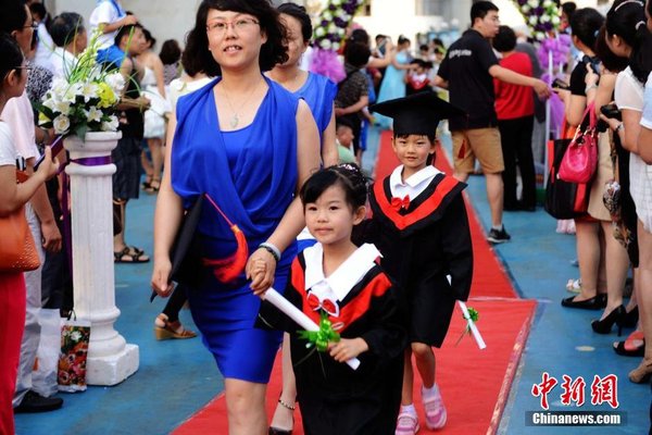 6月28日，山东青岛开发区第一幼儿园怡和嘉园分园2014级大班举行毕业典礼，全体毕业生身着学士服在盛装父母的陪同下，依次走过红毯，在毕业榜上郑重签下自己的名字，其气势不输当红影星红毯秀。中新社发 俞方平 摄 图片来源：CNSPHOTO