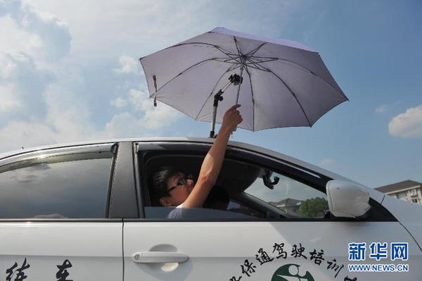 7月20日，在浙江省临安市一家驾校内，一名学员在车顶架着遮阳伞的教练车内练习。