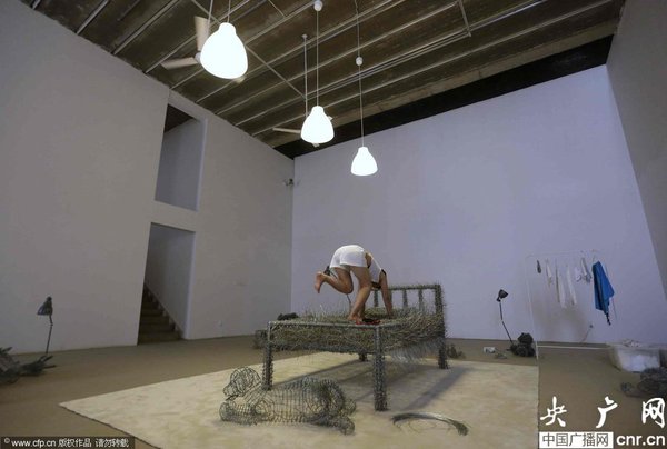 　2014年8月11日，北京，中国女艺术家周洁在北京现在画廊的展厅睡在一个未完成的铁丝床上，这一艺术项目被命名为“36天”，而这36天里，她可以正常进食、洗漱、如厕，以及玩手机等。