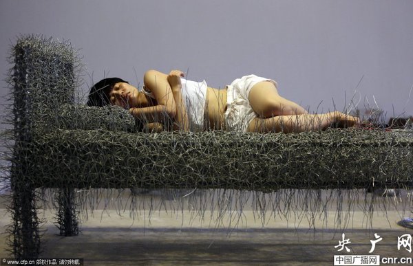 2014年8月11日，北京，中国女艺术家周洁在北京现在画廊的展厅睡在一个未完成的铁丝床上，这一艺术项目被命名为“36天”，而这36天里，她可以正常进食、洗漱、如厕，以及玩手机等。