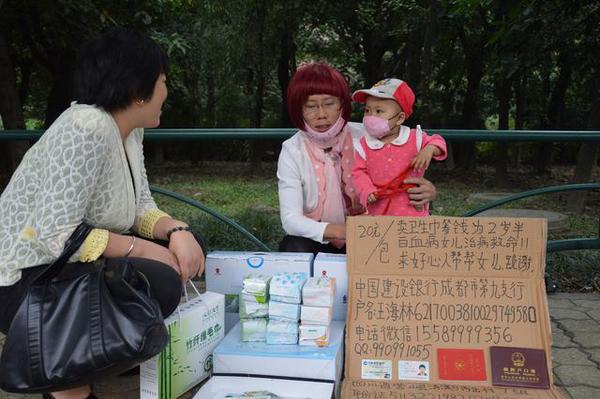 2014年10月8日下午，在成都市金牛区羊犀立交南某高档小区外，一名小女孩坐在路边，面前摆了几种不同颜色的某品牌卫生巾。一位女扮男装的中年男子称为了给得白血病的女儿治病，而在路边卖卫生巾筹钱。图为热心市民上前询问情况。