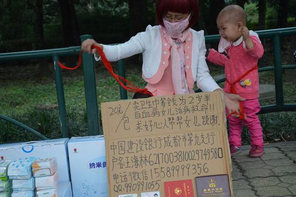 王海林的摊位前面摆放着一张纸板，上面写着“20元一包卖卫生巾，筹钱为白血病女儿治病”等内容，并粘着一张身份证和联系方式。为了防止孩子走失，王海林用绳子将孩子和他拴在一起。图为王海林为女儿系绳子。