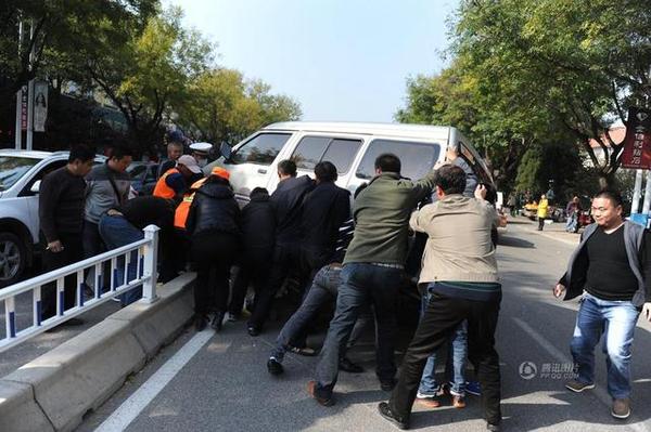 此时周围路过的市民和附近商贩纷纷赶来，十几人用力抬起面包车，将老人救出。