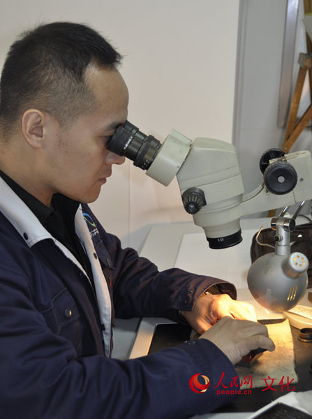 雕刻师正通过高倍放大镜,手持刀具在一块小小的钢版上,用手工雕刻出与邮票票面同样大小的部分图案。(人民网 王鹤瑾 摄)