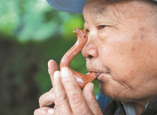 万富册老人为过往市民吹奏泥鹅子。