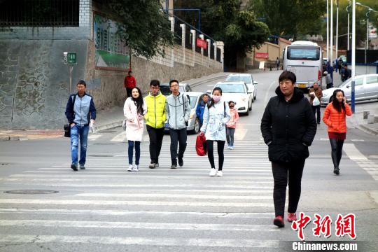 图为市民们穿着棉服、羽绒服在寒风中卷缩着过马路。　孙睿 摄