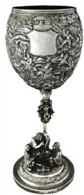 征战图高脚杯   Standing Trophy with Battle Scene Pattern 晚清 通高：29cm；口径：9.5cm；底径：10.6cm；重:681g 款识：慎昌，LW   清代中晚期，随着外销银器的逐渐升温，银匠不仅开始借鉴青铜器、瓷器的特征创造银器，更融合进宗教思想及丰富的想象力。征战图高脚杯的杯身运用锤揲工艺由内向外敲击出隋唐故事“罗通扫北”浮雕图，在杯身中央位置留有一醒目光面盾牌，用以錾刻购买者家族族徽，一方面彰显其身份地位，另一方面也能够起到防盗的作用。整体造型极具艺术感，杯托被设计成一只展翅翱翔的雄鹰，杯杆被设计成配有圆环的锡杖造型。底座焊接一打坐罗汉和一伏虎抱杵罗汉，底座整体设计成须弥山的造型，须弥山在印度佛教中象征着世界之中心，整体做工精湛，布局巧妙，体现了银匠的艺术造诣与佛教思想的融合。