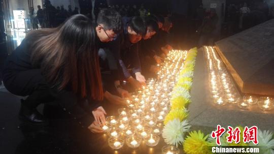 12月13日，沈阳“九一八”历史博物馆在国家公祭日举行悼念仪式。图为民众向寓意民族英烈浩气长存的金字塔型卧碑敬献烛火。　朱明宇 摄