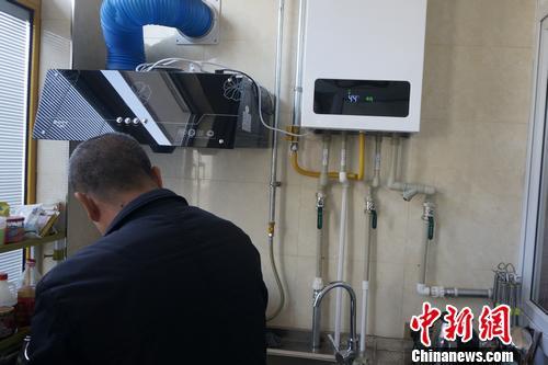 山西某村民正用燃气灶烧水，一旁的壁挂炉显示供暖温度。汤琪 摄