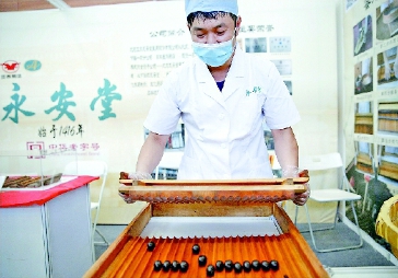 ▲图为工作人员在活动现场向观众展示中药蜜丸制作工艺。