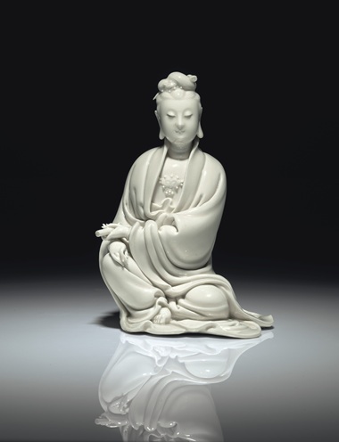 明十七世纪初 德化白釉书卷观音坐像 《何朝宗》葫芦形印款，高8 58 寸 (21.9公分)。估价：60,000-80,000美元。此拍品于2018年9月13至14日在佳士得纽约亚洲艺术周之中国瓷器及工艺精品拍卖中呈献。