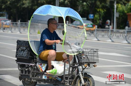 资料图：男子在电动车上撑起遮阳棚。<a target='_blank' href='http://www.chinanews.com/'>中新社</a>记者 刘文华 摄