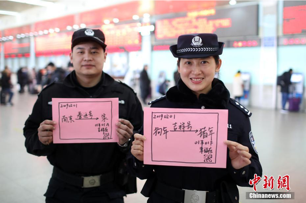 2月1日，随着春节临近，南京铁路公安处南京站派出所的民警在纸上写下“平安春运，有我们护航”、“天下无贼是我们最大的心愿”、“平安归途么么哒”等话语，用别样的方式给旅客们送上温馨的新年祝福。图为南京火车站售票大厅内的值班民警和特勤送出温馨祝福语。中新社记者 泱波 摄