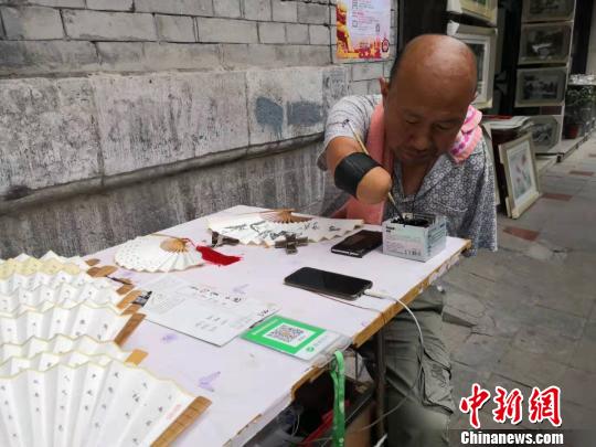 贾维军坐在自己的简易摊位前写字。　阿琳娜 摄