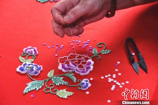 在绣工的穿针引线下，花朵逐渐“绽放”在罗缎上。　陈龙山 摄
