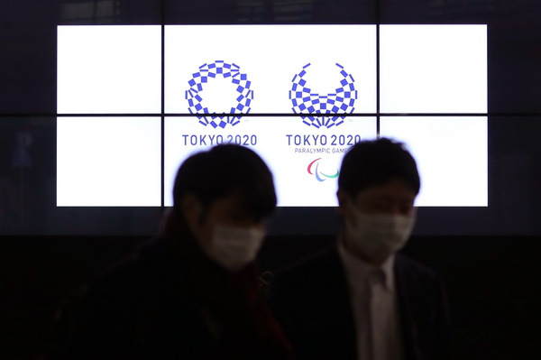 3月30日，在日本东京新桥，行人经过显示东京奥运会和残奥会会徽的电子屏。